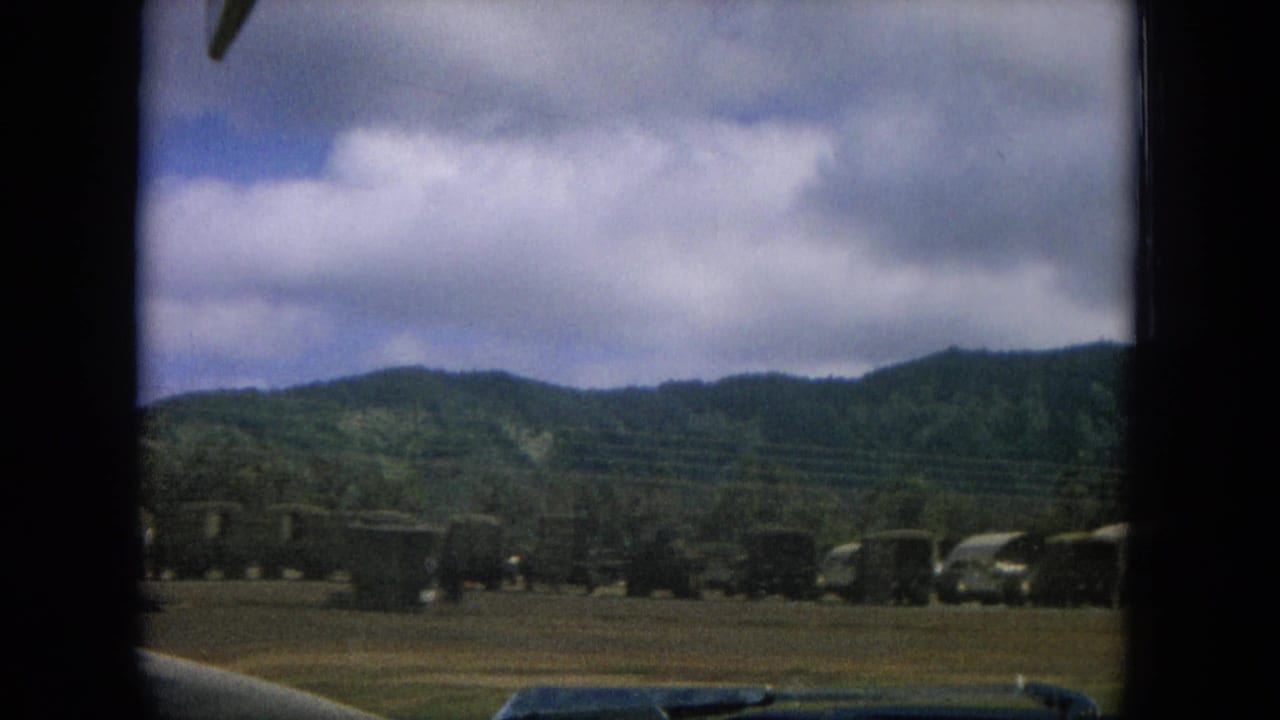 1964 8mm roadside view in Oahi, Hawaii, showing open land, low hills, cloudy sky, and passing foreground obstruction.