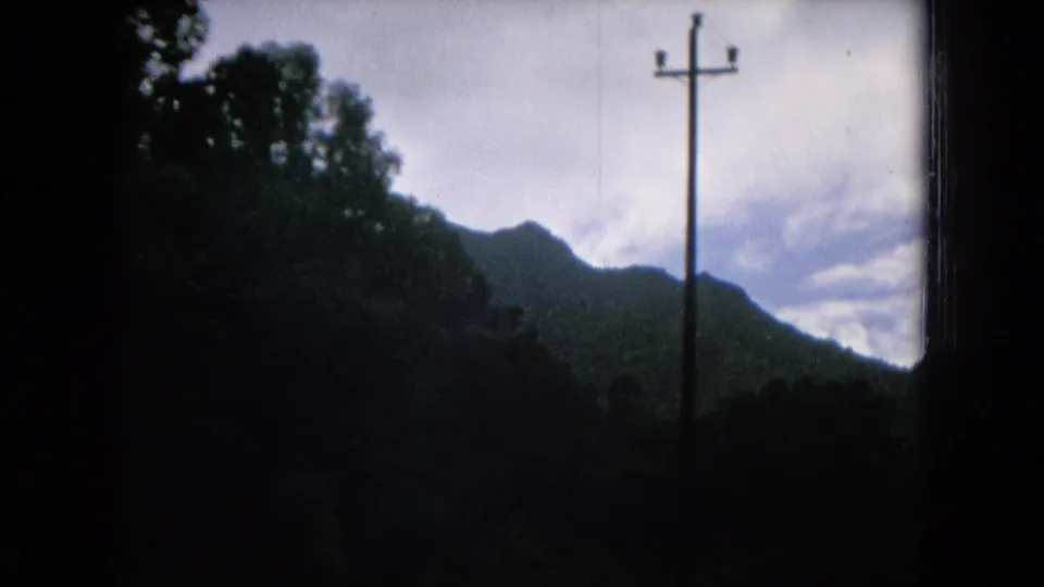 1964 Hawaii rural roadside frame with a utility pole, dark tree line, and distant mountain ridge under clouds.