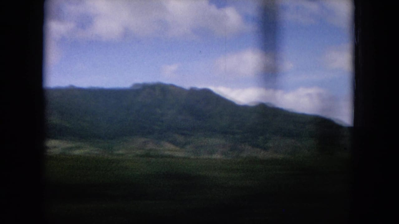 Oahu landscape view with a broad green ridge, valley slopes, blue cloudy sky, and dark vehicle-window borders.