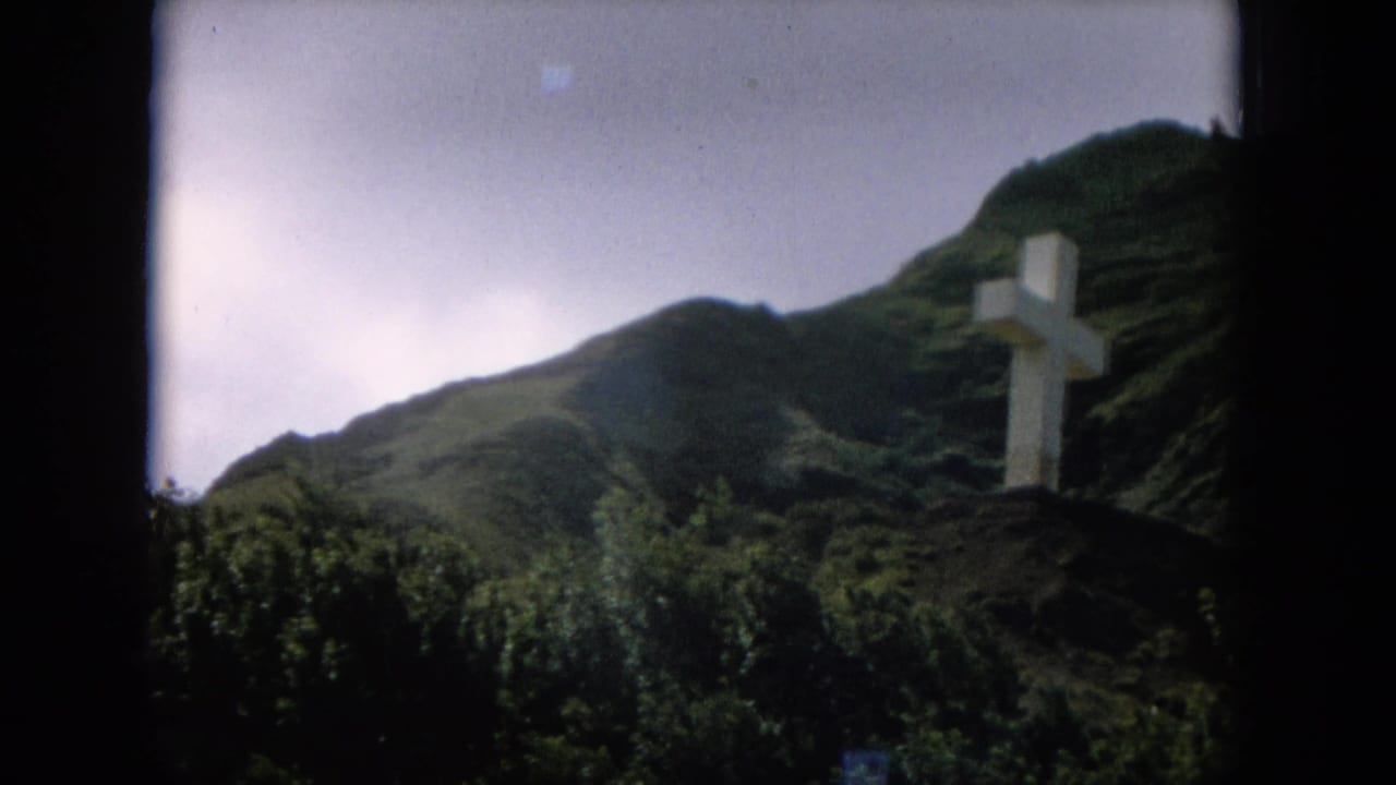 Large white cross on a green mountain slope under an overcast sky.