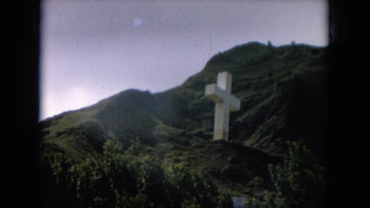 White cross viewed from a distance against steep green hills.