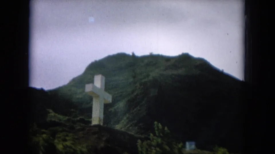 Final 1964 8mm frame holding on the white cross beneath a green ridgeline in Oahi, Hawaii.