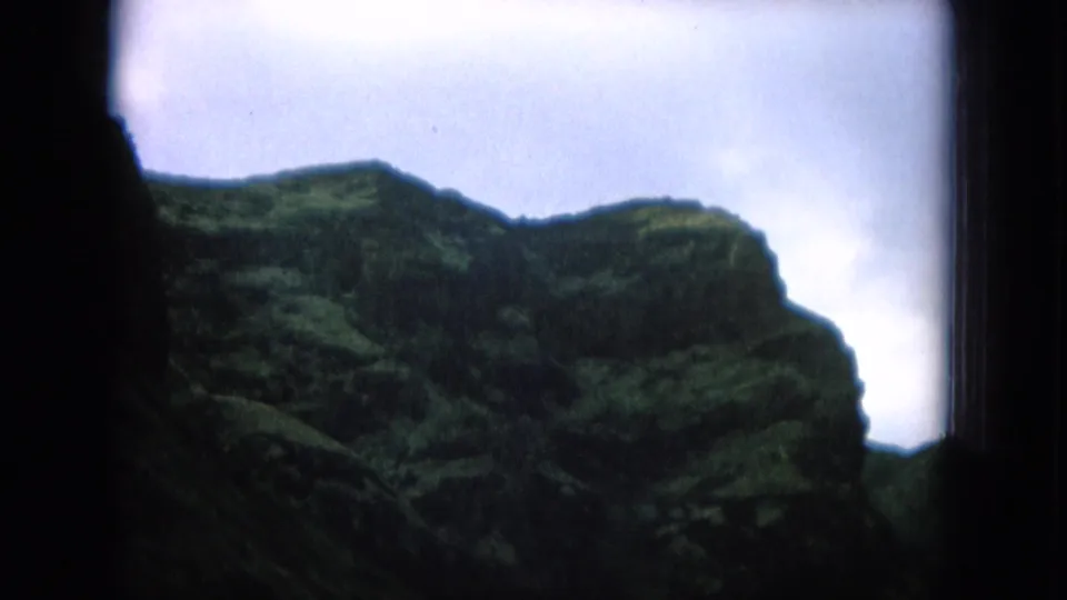 Soft 8mm Hawaii frame showing steep green Oahu mountain slopes close to the camera, with pale sky and dark framing at the edges.