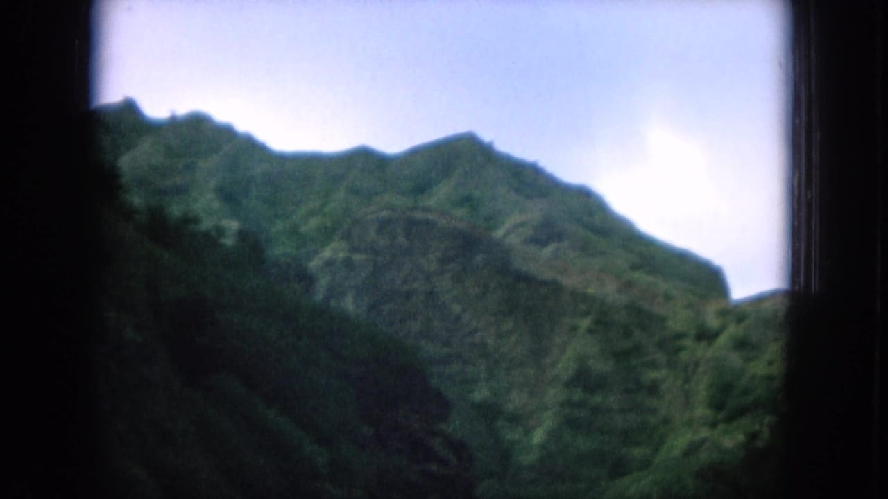 Green mountain ridge seen through dark vehicle-window framing.