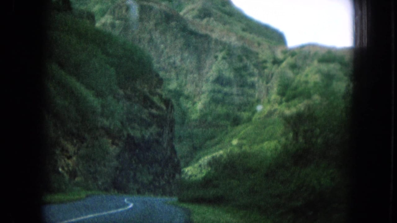 Winding road below steep green mountains and dense foliage.