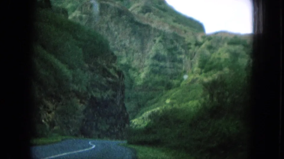 A curving road passes through steep, green Oahu mountain terrain in 1964 8mm home-movie footage.