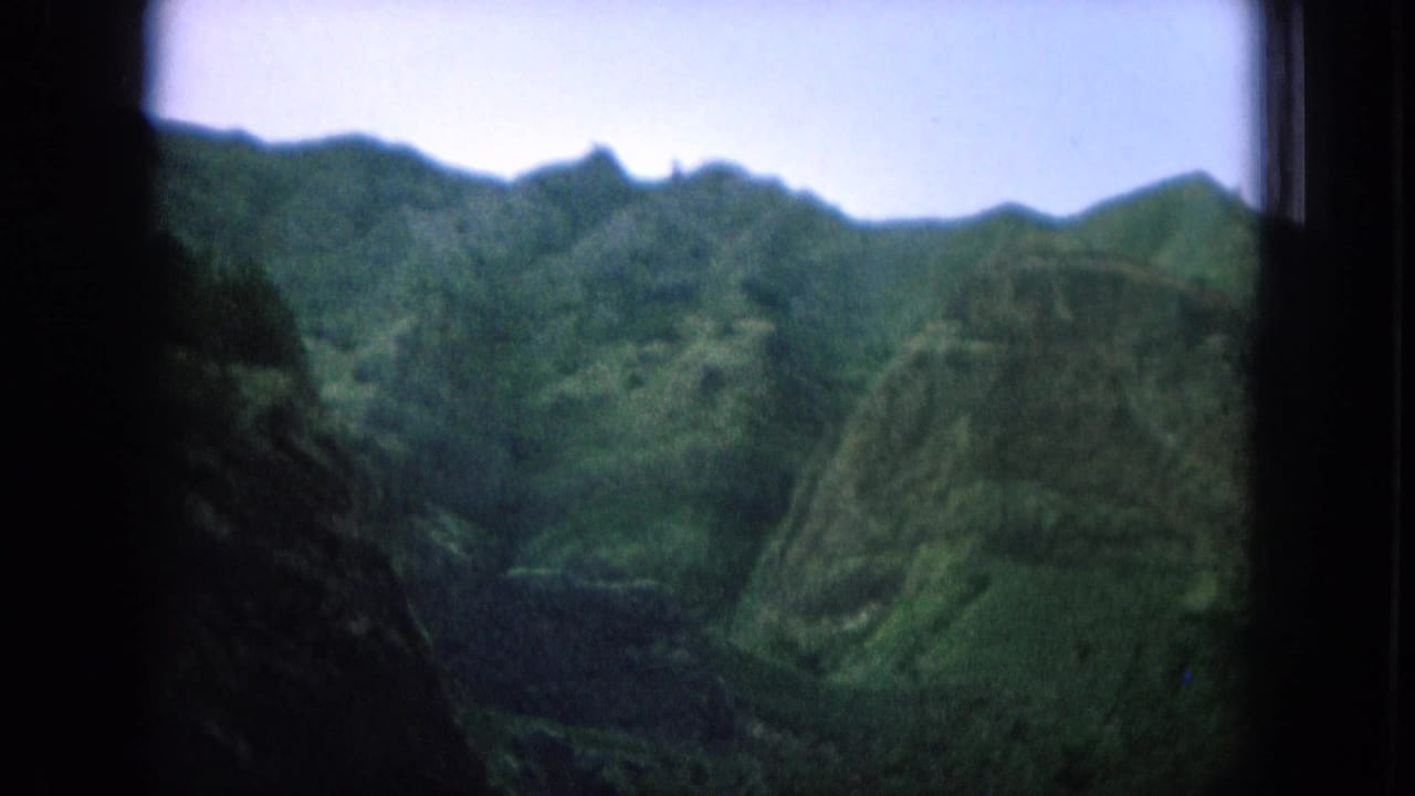 1964 8mm Hawaii travel frame showing lush mountain ridges through a dark window frame with soft focus and muted color.