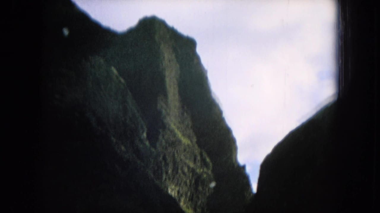 1964 Hawaii home-movie frame with a steep green mountain face partly silhouetted between dark window borders.