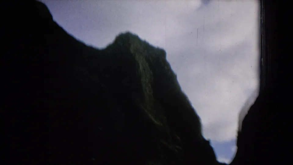 1964 Hawaii travel frame showing a shadowed rugged ridge with green highlights near a pale sky and dark window border.