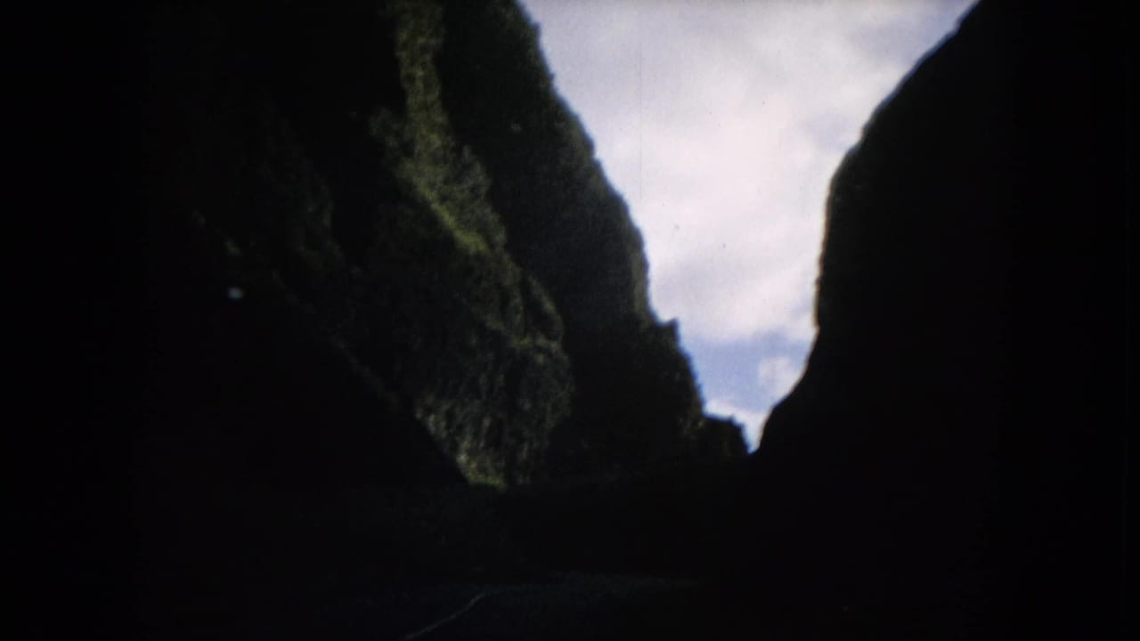 1964 Hawaii 8mm frame looking through steep green canyon walls toward a pale cloudy opening ahead.