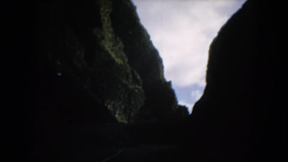 1964 Hawaii 8mm frame looking through steep green canyon walls toward a pale cloudy opening ahead.