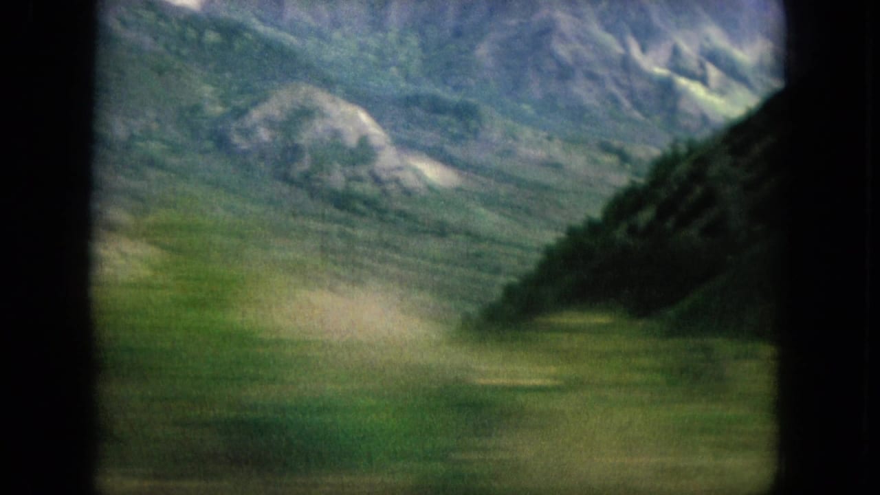 Green valley and mountains seen from a moving vehicle.