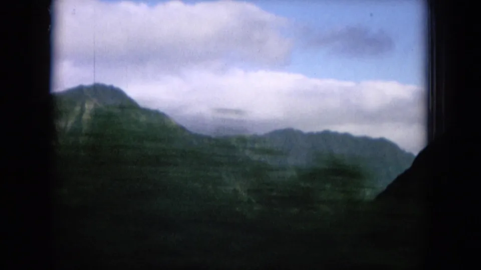 1964 Hawaii home-movie frame showing cloudy mountain ridges beyond dark foreground canyon edges.