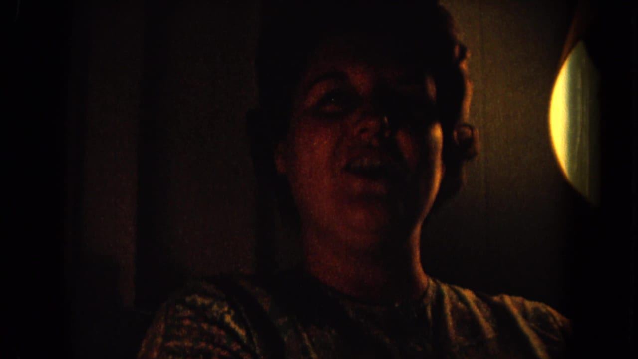 1964 Hawaii home-movie frame of an adult woman laughing in a dim room, with a circular bright light at the right edge.