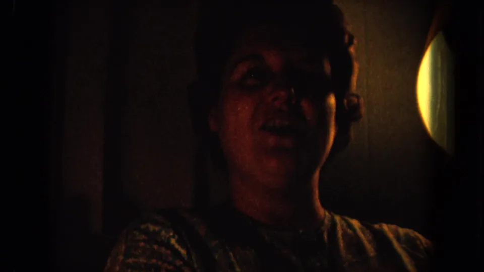 1964 Hawaii home-movie frame of an adult woman laughing in a dim room, with a circular bright light at the right edge.
