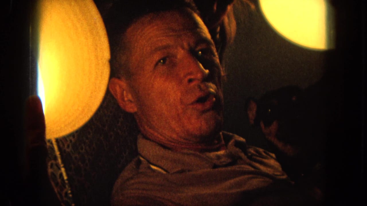 Close view of a man singing beside warm round lights in a dark interior.