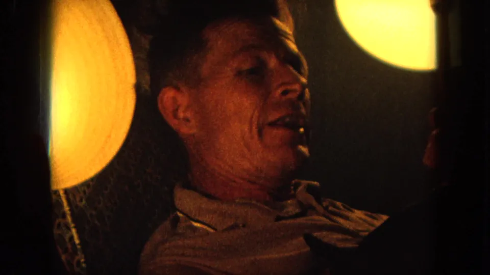 Close 8mm view of the male singer in a dim venue, with amber lighting and visible film grain.