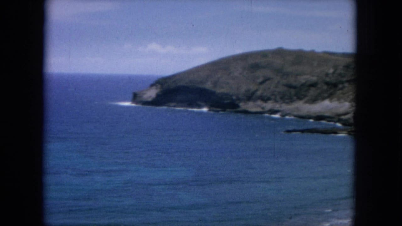 1964 8mm Oahu coastal view looking across blue Pacific water toward a rocky headland and dry green hills.