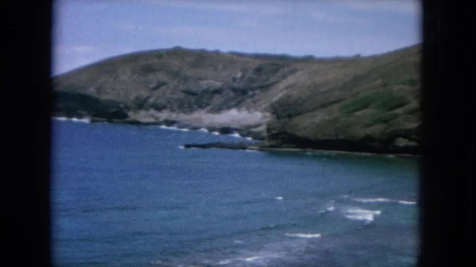 1964 Oahu shoreline seen from above, with rocky slopes, blue water, and small surf breaks along the coast.