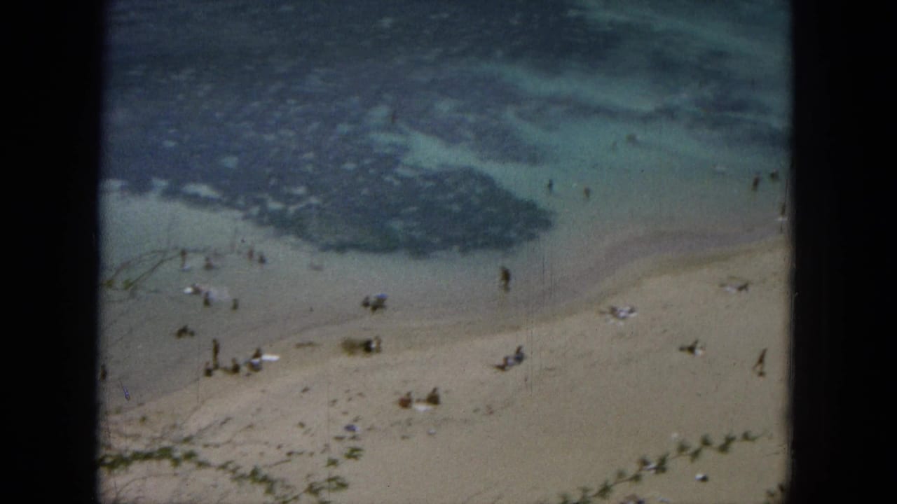 Elevated 1964 Hawaii beach view showing scattered people in the surf zone and on the sand, seen through dark 8mm frame edges.