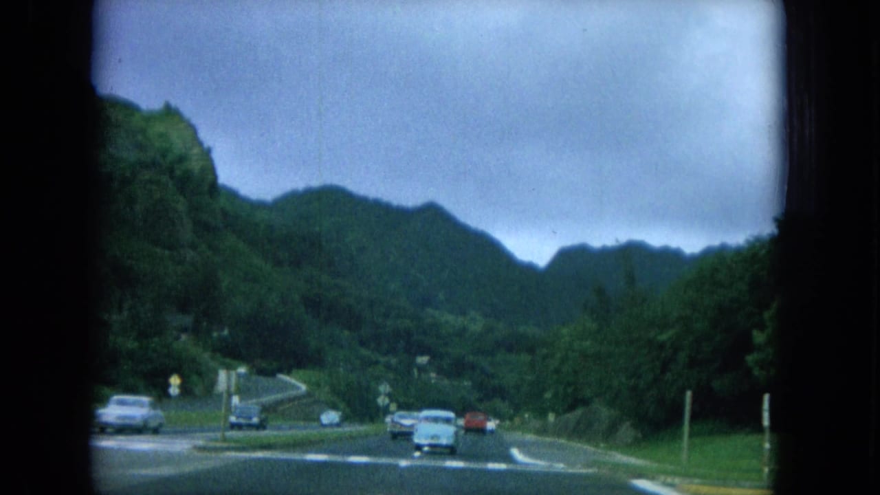 Winding highway with several cars, green mountains, and roadside signs.