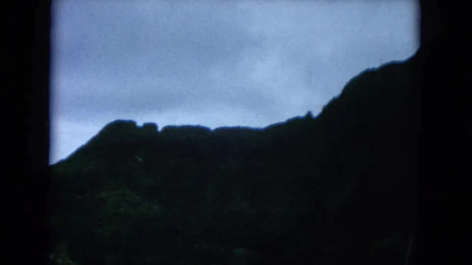 A dim 8mm frame from the Hawaii road trip shows mountain silhouettes, foliage, and a partial vehicle-window obstruction.