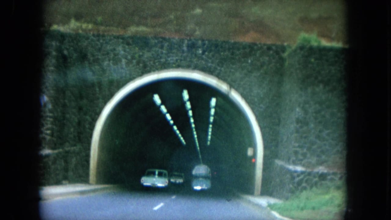 Cars drive into a lit tunnel entrance framed by stonework.