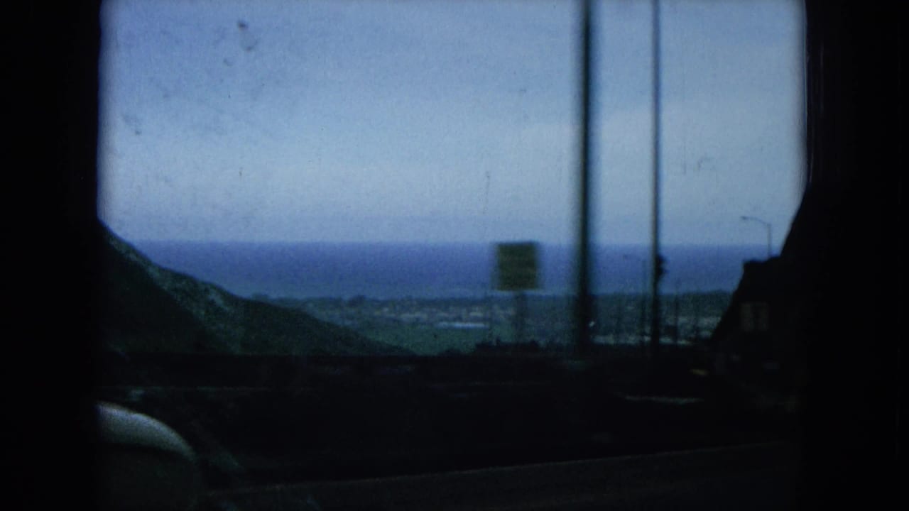 Oahu coastal approach seen through a car window, with poles, a roadside sign, dark foreground, and hazy ocean beyond.