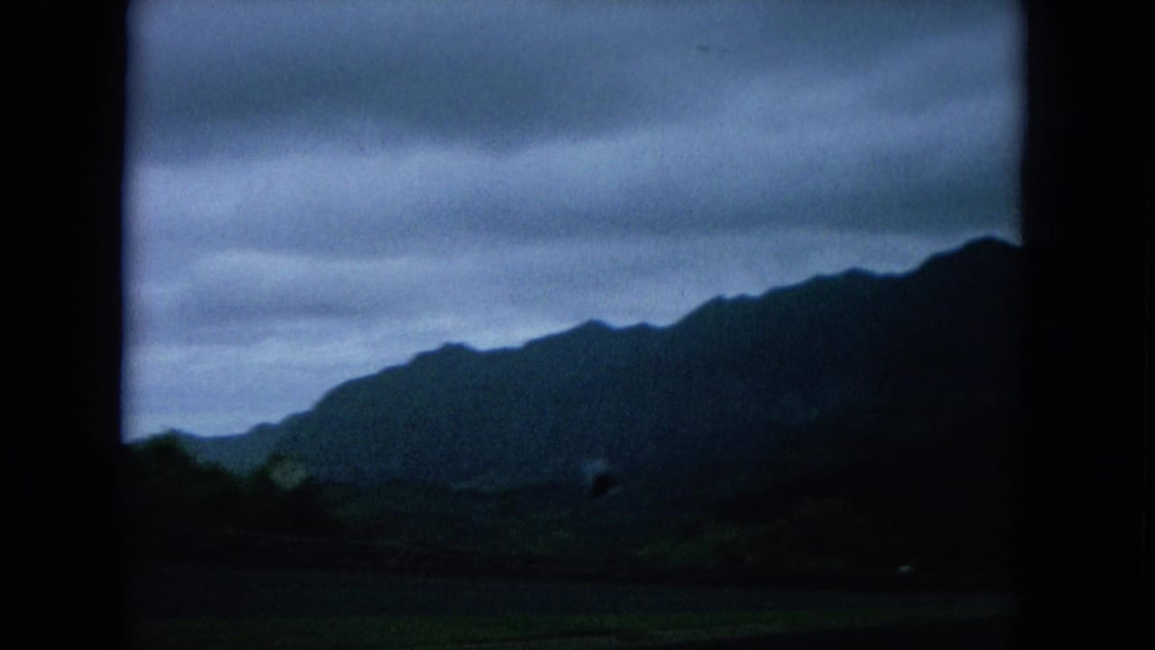 Oahu landscape framed by a vehicle window, with mountain slopes and low clouds in soft 8mm color.