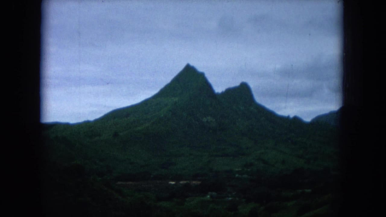 Green mountain ridge under a cloudy sky, seen from a moving vehicle.