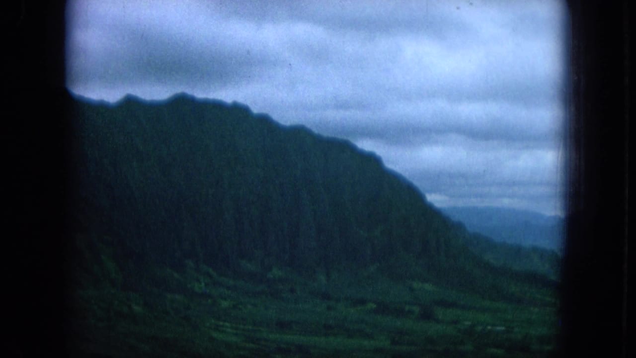 1964 Oahu footage frames a steep forested ridge and valley edge in cool, cloudy light from a sheltered viewpoint.
