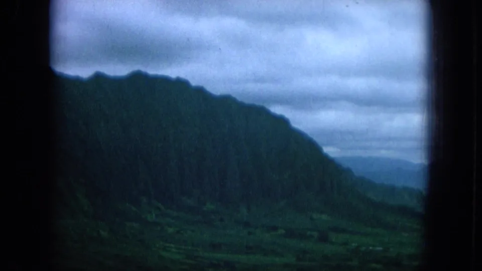 1964 Oahu footage frames a steep forested ridge and valley edge in cool, cloudy light from a sheltered viewpoint.