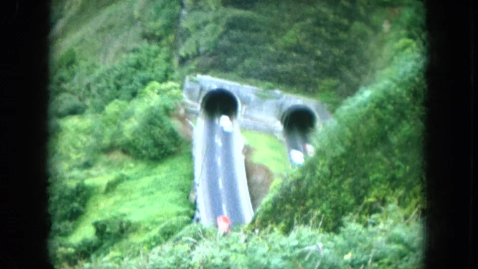 1964 Oahu home-movie view of a concrete road tunnel set into lush hillside vegetation, with a car visible inside an opening.