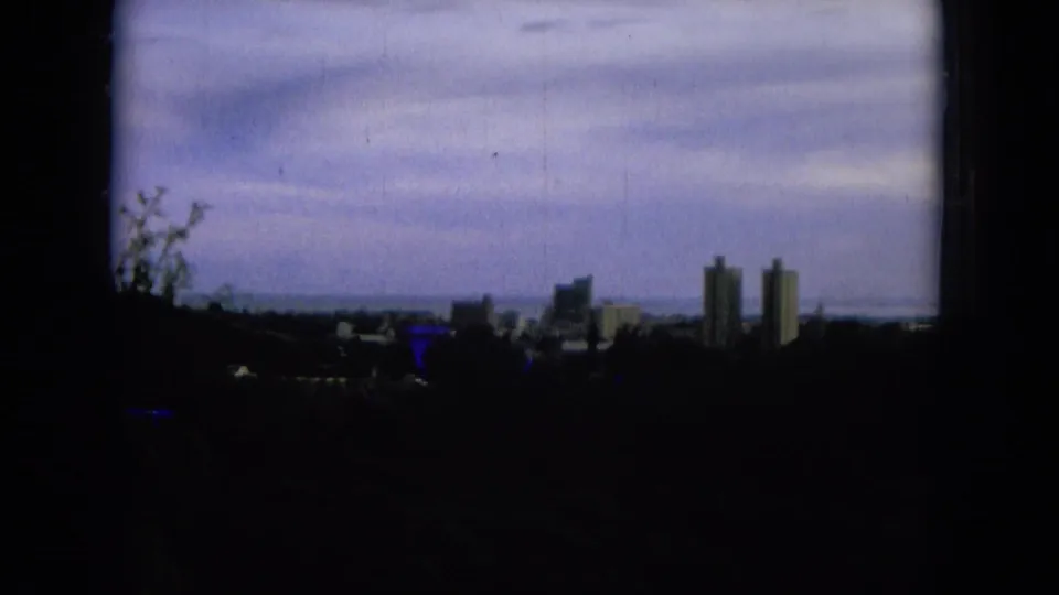 1964 Hawaii 8mm frame with silhouetted hillside, distant tower blocks, coastal horizon, and blue-green film color cast.