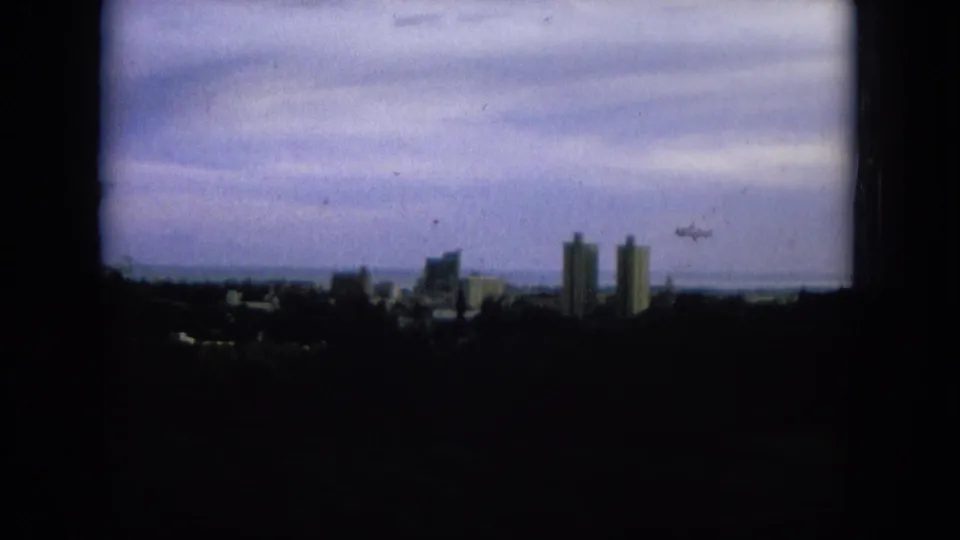 1964 8mm view of a distant Oahi, Hawaii skyline under a heavy overcast sky, with towers silhouetted above a dark foreground.