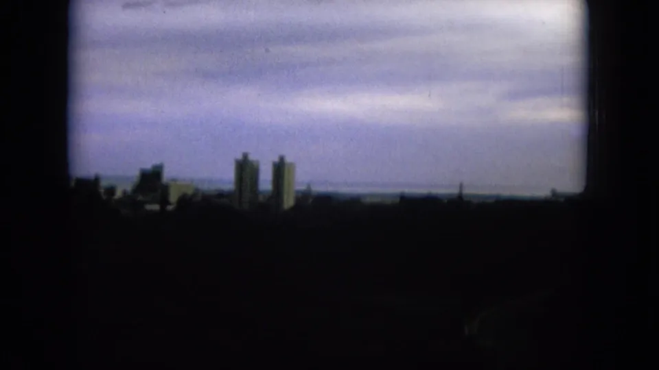 Soft 8mm frame of the Oahi, Hawaii skyline, with two prominent towers, a low horizon, and darkened foreground under cloud cover.