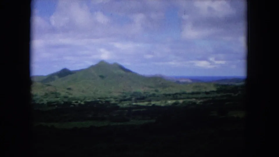 1964 Oahi, Hawaii 8mm frame showing a wide mountain range and valley landscape beneath a clouded blue sky.