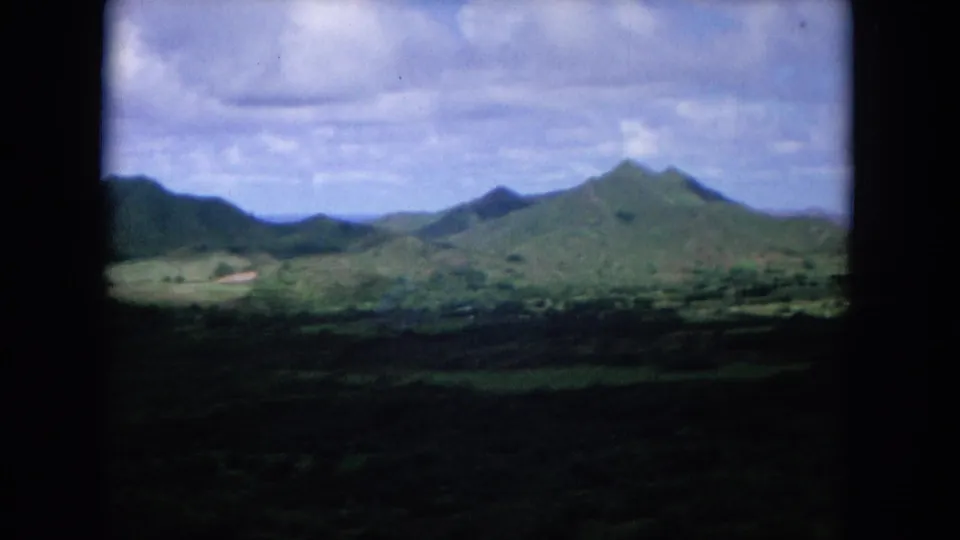 1964 Oahi, Hawaii 8mm frame with rolling hills, pointed mountain peaks, and a broad partly cloudy sky.