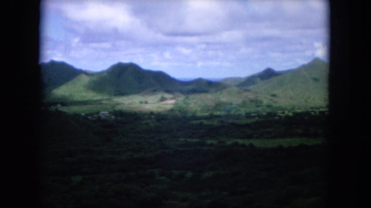 1964 Oahu home-movie view of green mountain ridges and a broad valley beneath a partly cloudy sky, framed by dark film edges.