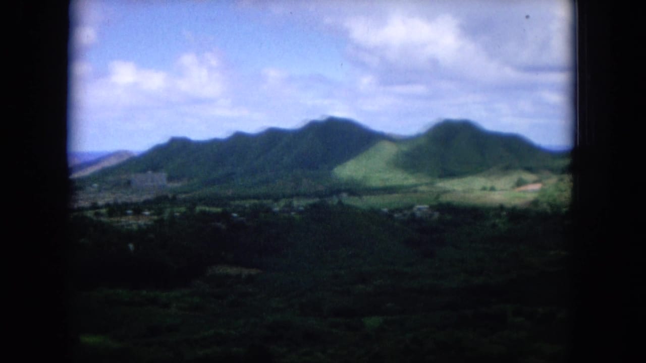 Mountain ridge and green valley with distant settlement beneath clouds.