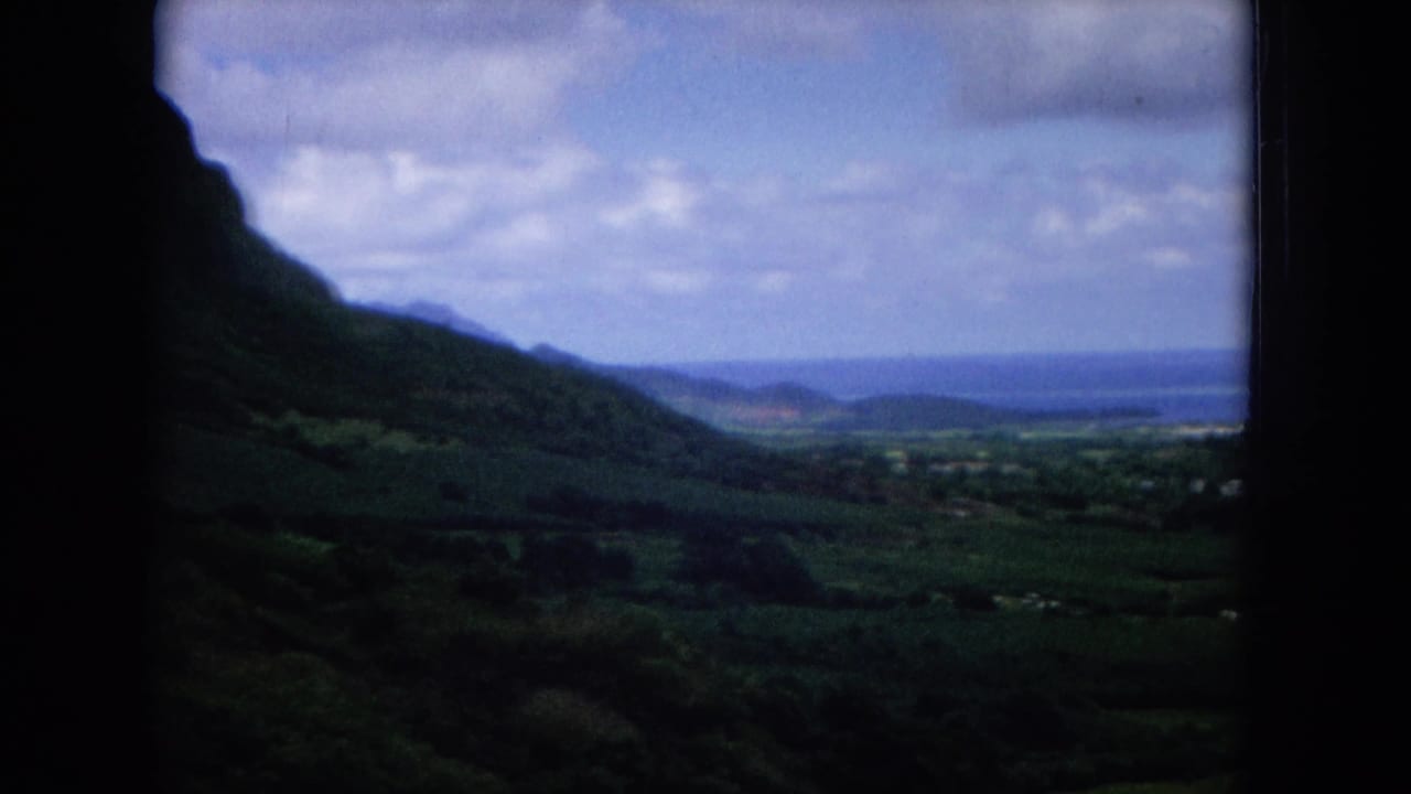 1964 8mm home-movie view of an Oahu mountain valley through a vehicle window, with distant water under clouds.