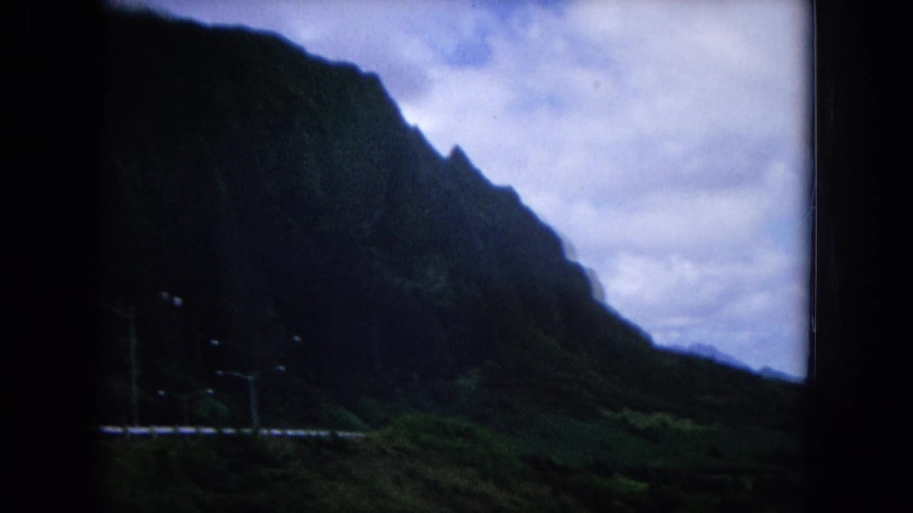 Dark mountain ridge beside a road with streetlights under a cloudy sky.