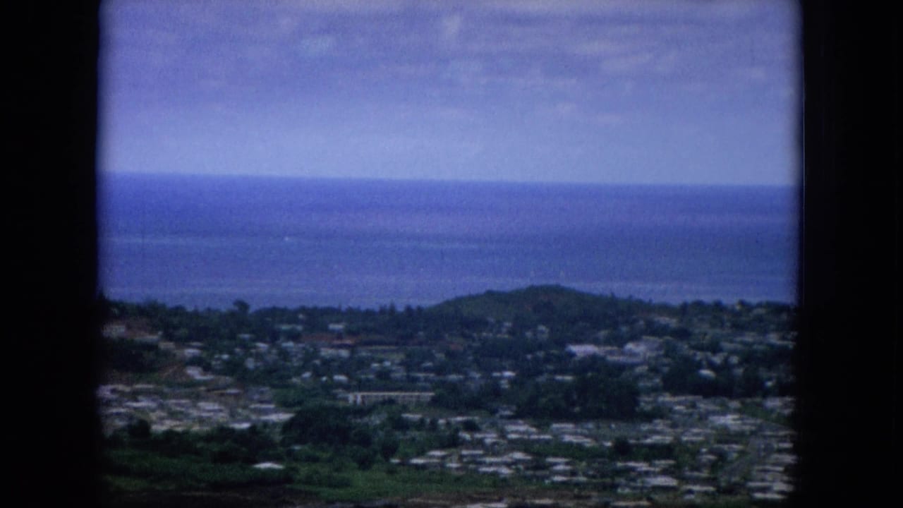 1964 Hawaii home-movie frame showing a soft elevated view over homes, roads, green hills, and the Pacific horizon.