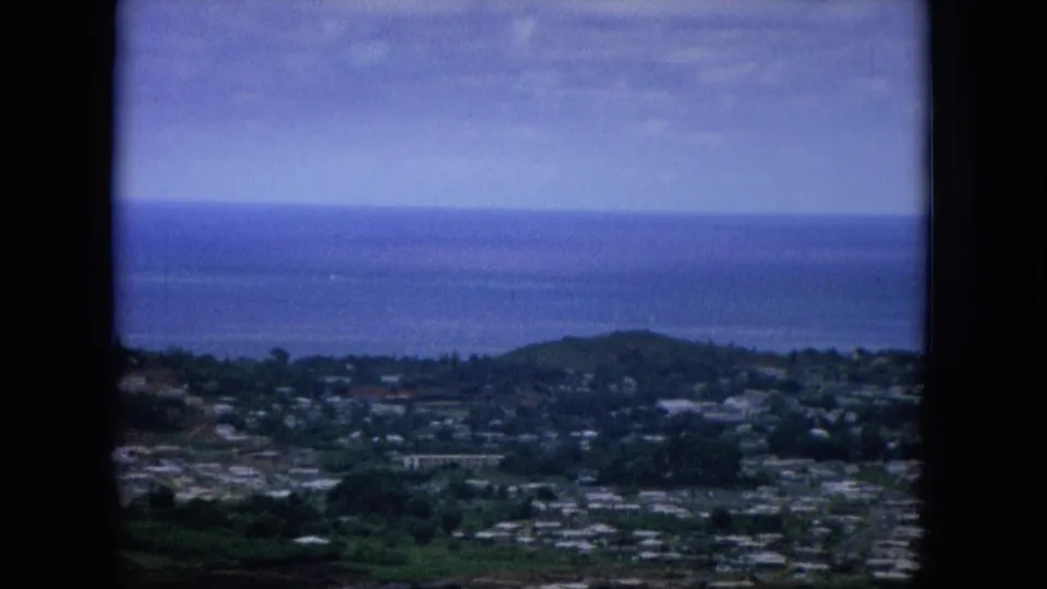1964 Hawaii home-movie frame showing a soft elevated view over homes, roads, green hills, and the Pacific horizon.