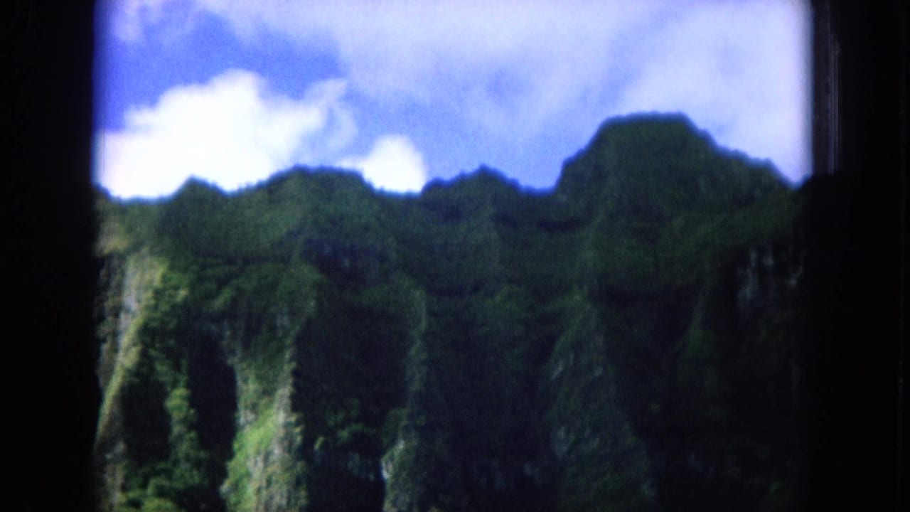 Forest-covered mountains and cliff shadows below a bright clouded sky.