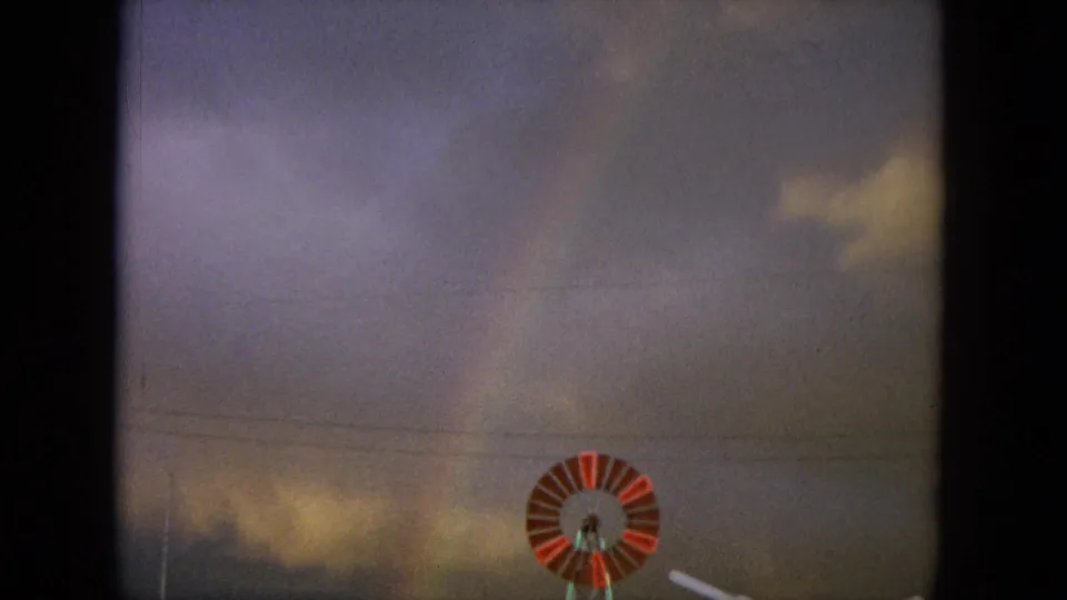 1964 Hawaii home-movie frame with the windmill partly visible below a cloudy sky and faint rainbow.