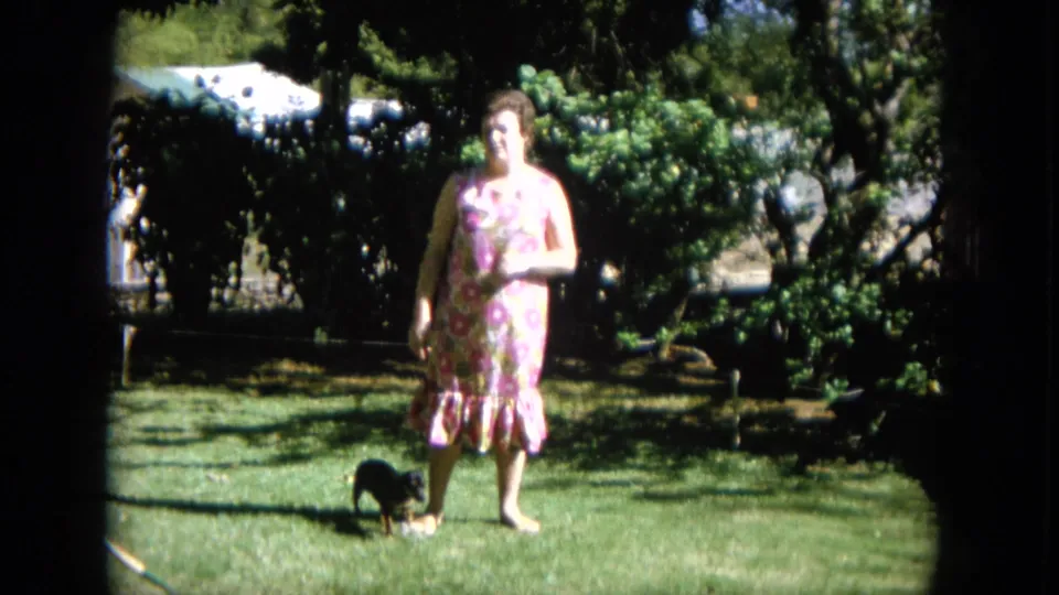 Adult woman in a floral dress stands in a sunlit garden in Oahi, Hawaii, with the small dog near her feet.