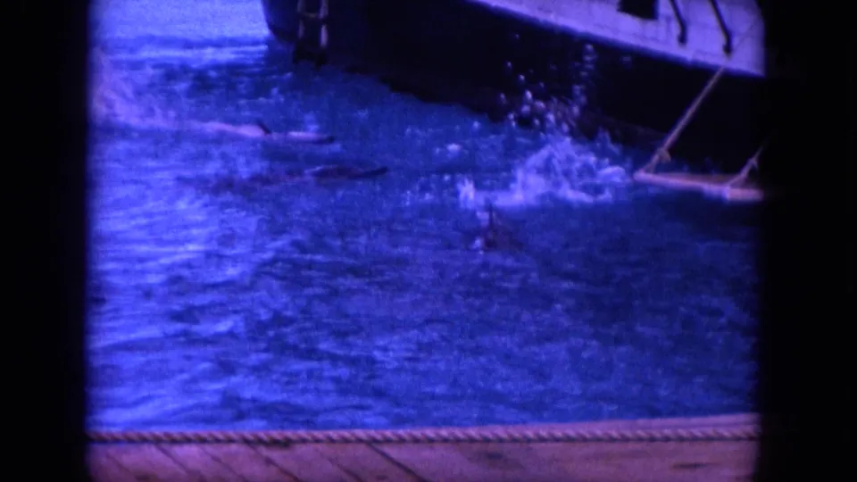 1964 Hawaii 8mm frame showing water beside a boat, with a dolphin or splash activity near the surface.