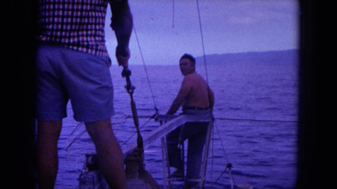 Two men on a small boat with open water and a distant shoreline behind them.