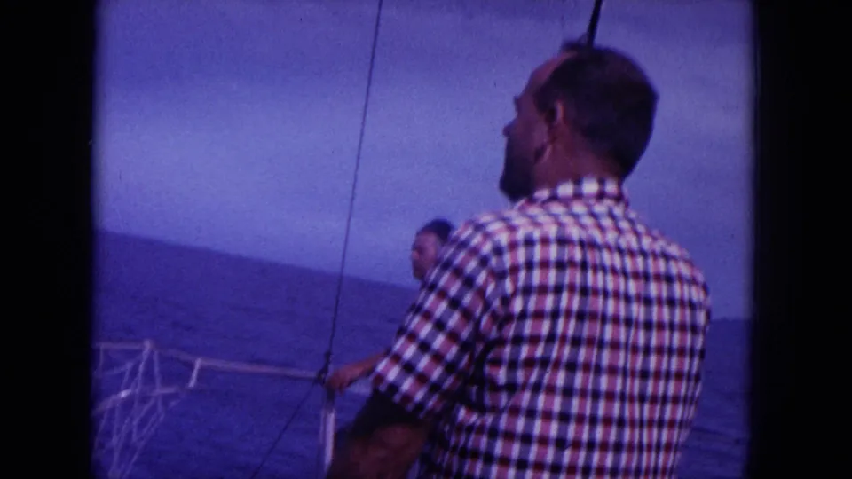 1964 Hawaii home-movie frame showing an adult man in a plaid shirt on a boat looking out over the ocean.